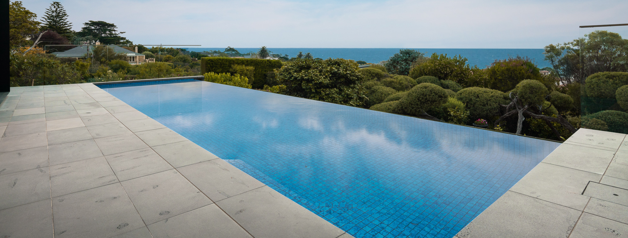 Infinity pool overlooking scenic trees and ocean, showcasing a luxurious and serene outdoor swimming environment.